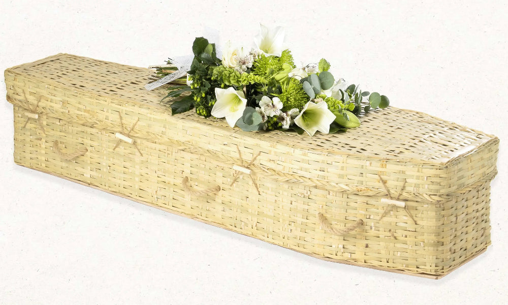 Ecoffins Bamboo Traditional wicker coffin with floral arrangement on a white background