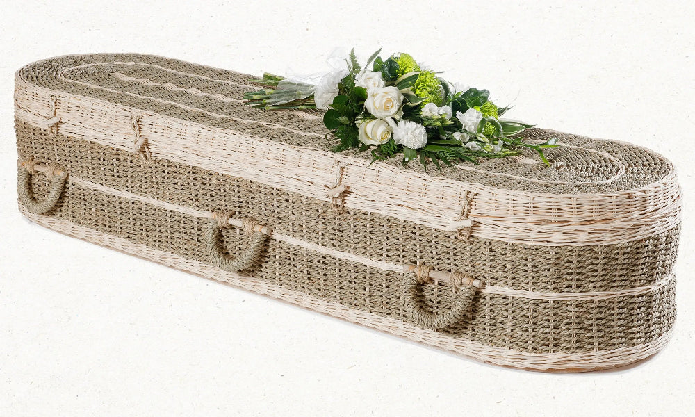 Ecoffins Pandanus Round wicker coffin with floral arrangement on a white background