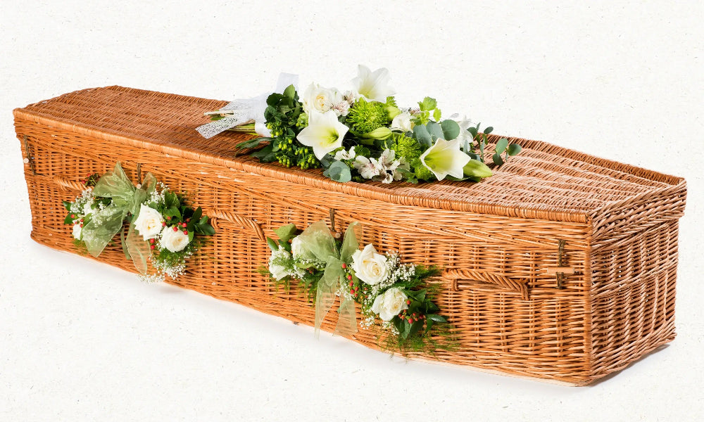 Ecoffins Willow Highsted wicker coffin with floral arrangements on a white background